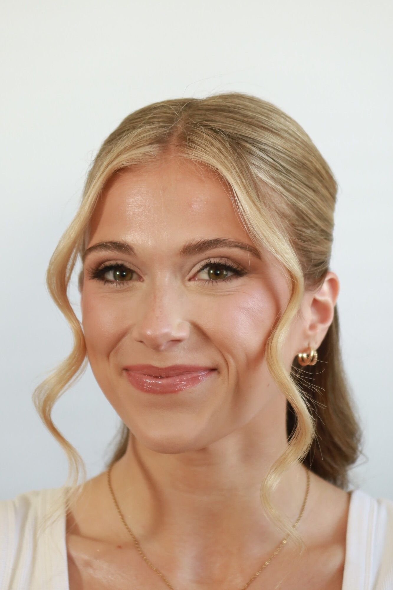 After: the same woman in soft glam makeup with half-up hair and face-framing waves