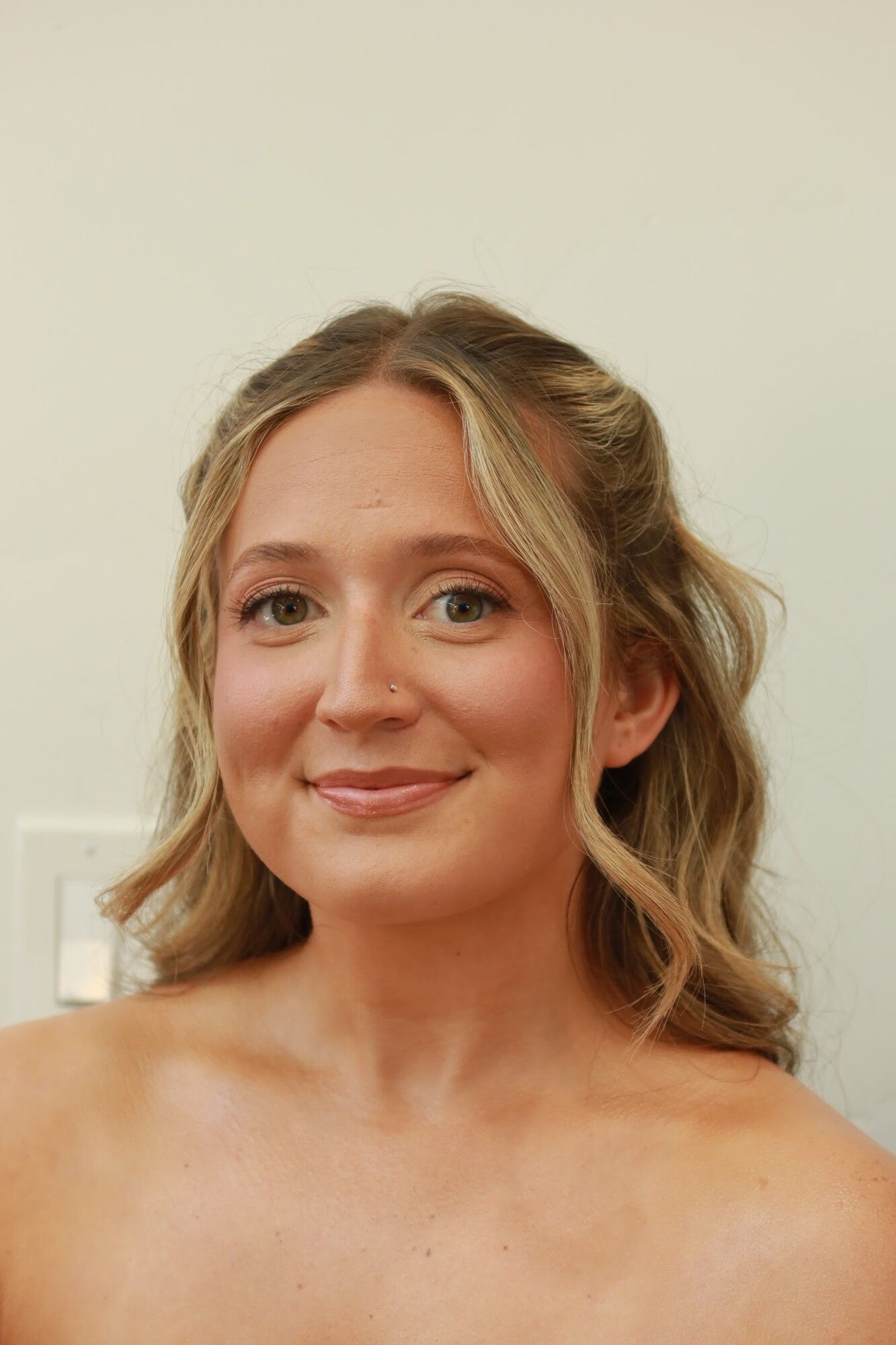 After: the same woman with half-up hair, soft waves and soft glam makeup