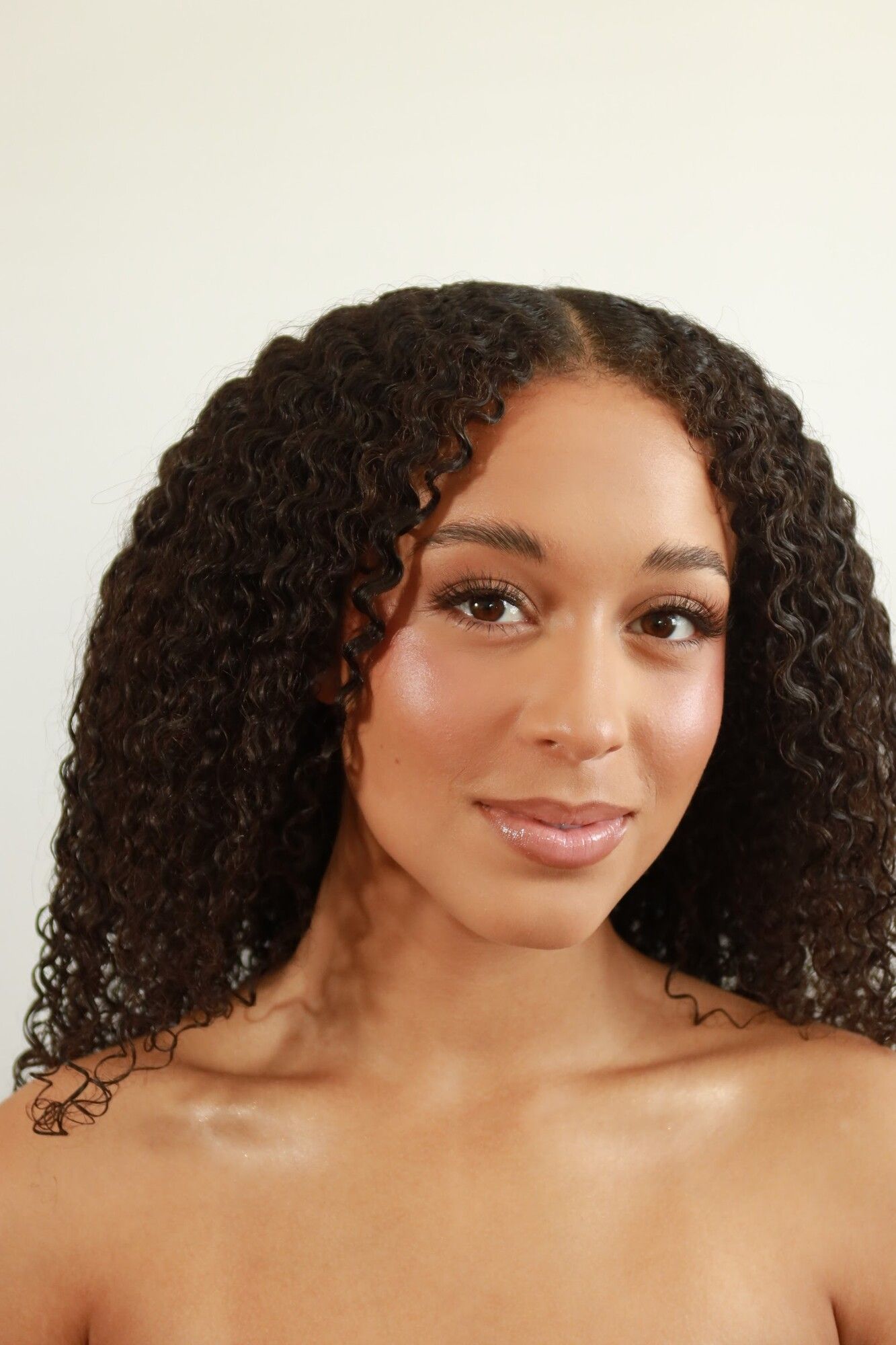 After: the same woman with defined curls and a glowing soft glam finish
