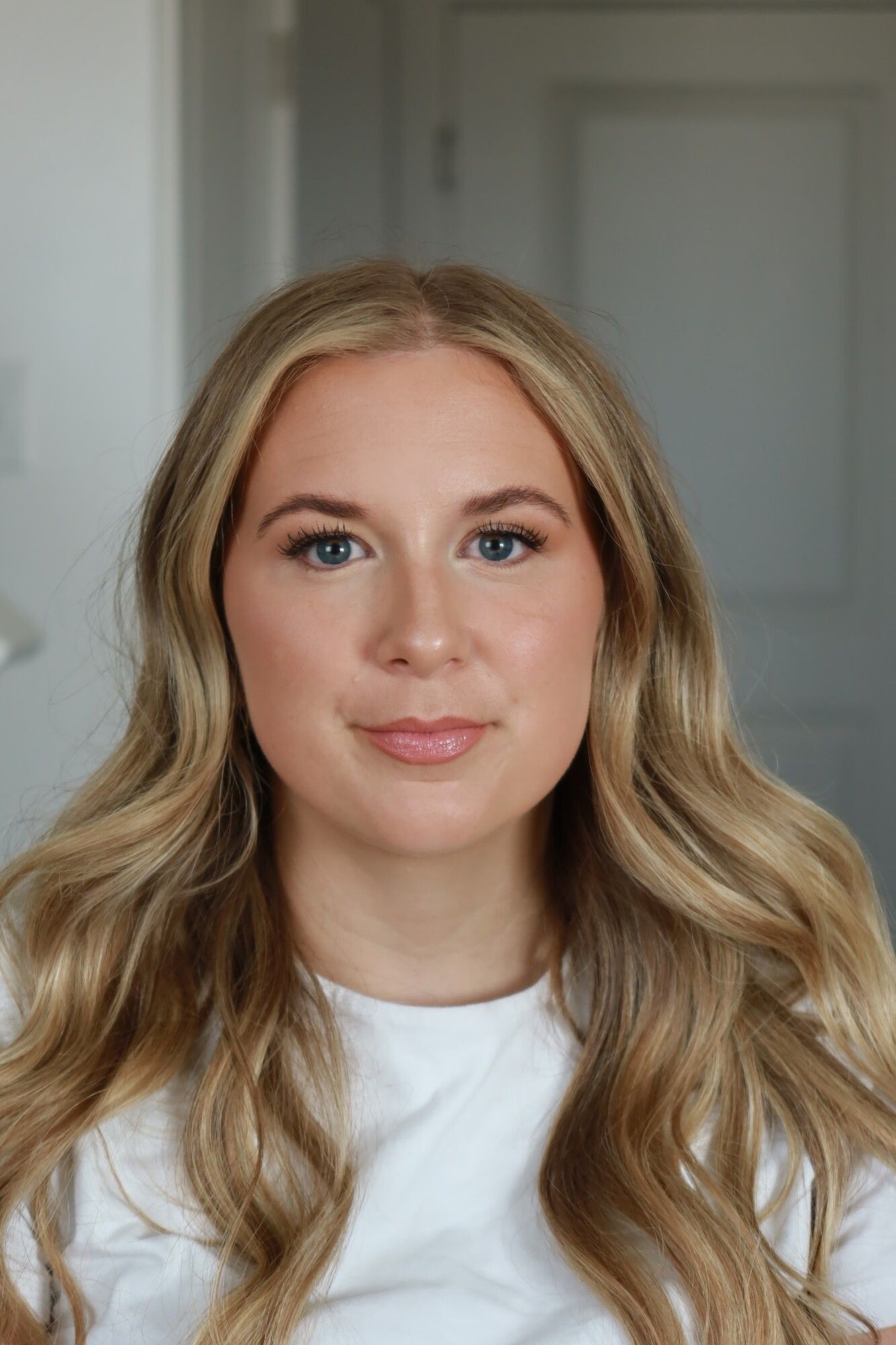 A blonde woman with long soft waves and finished bridal makeup in a white top