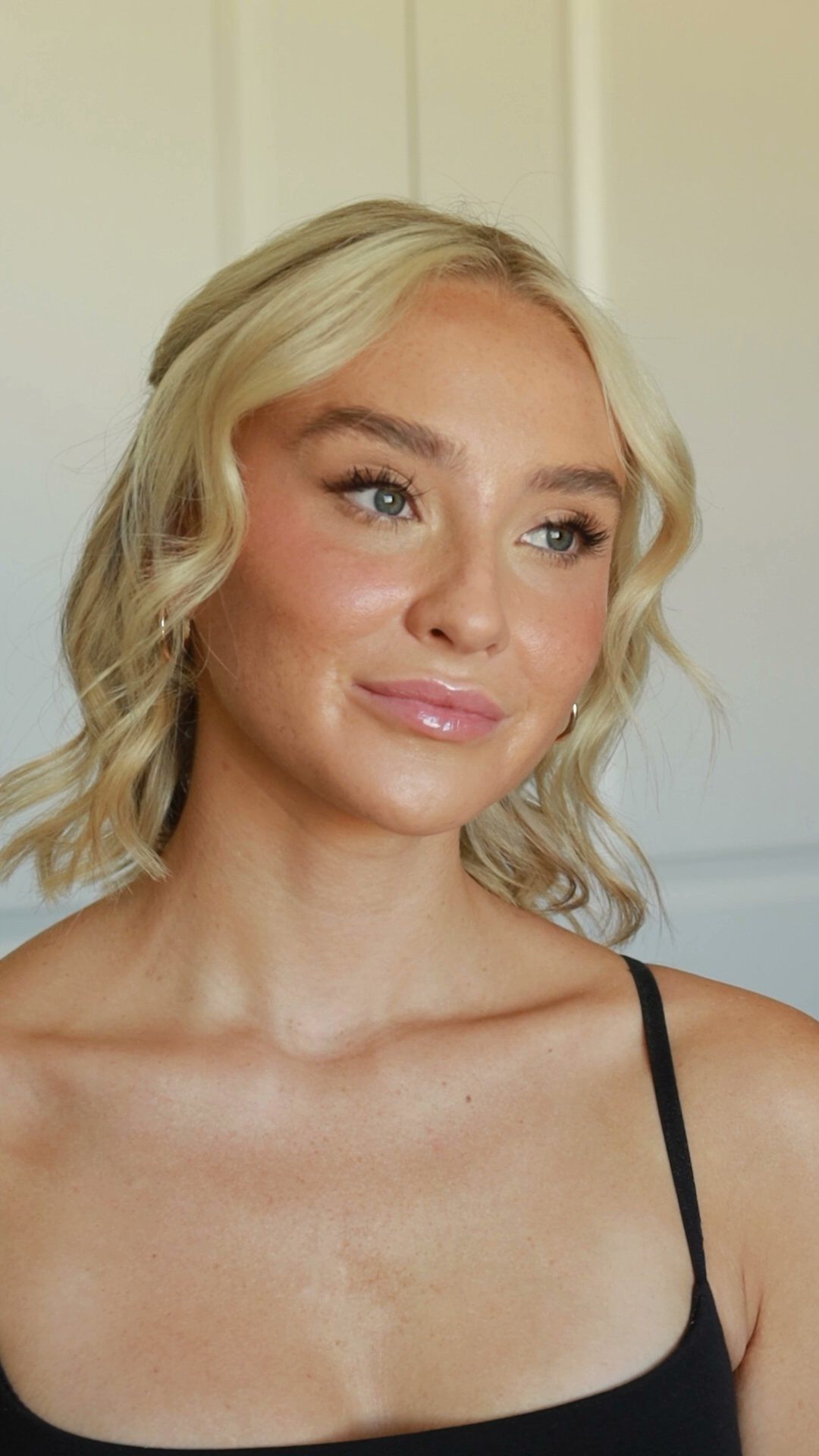 A blonde woman with wavy hair and glowing soft glam makeup in a black top