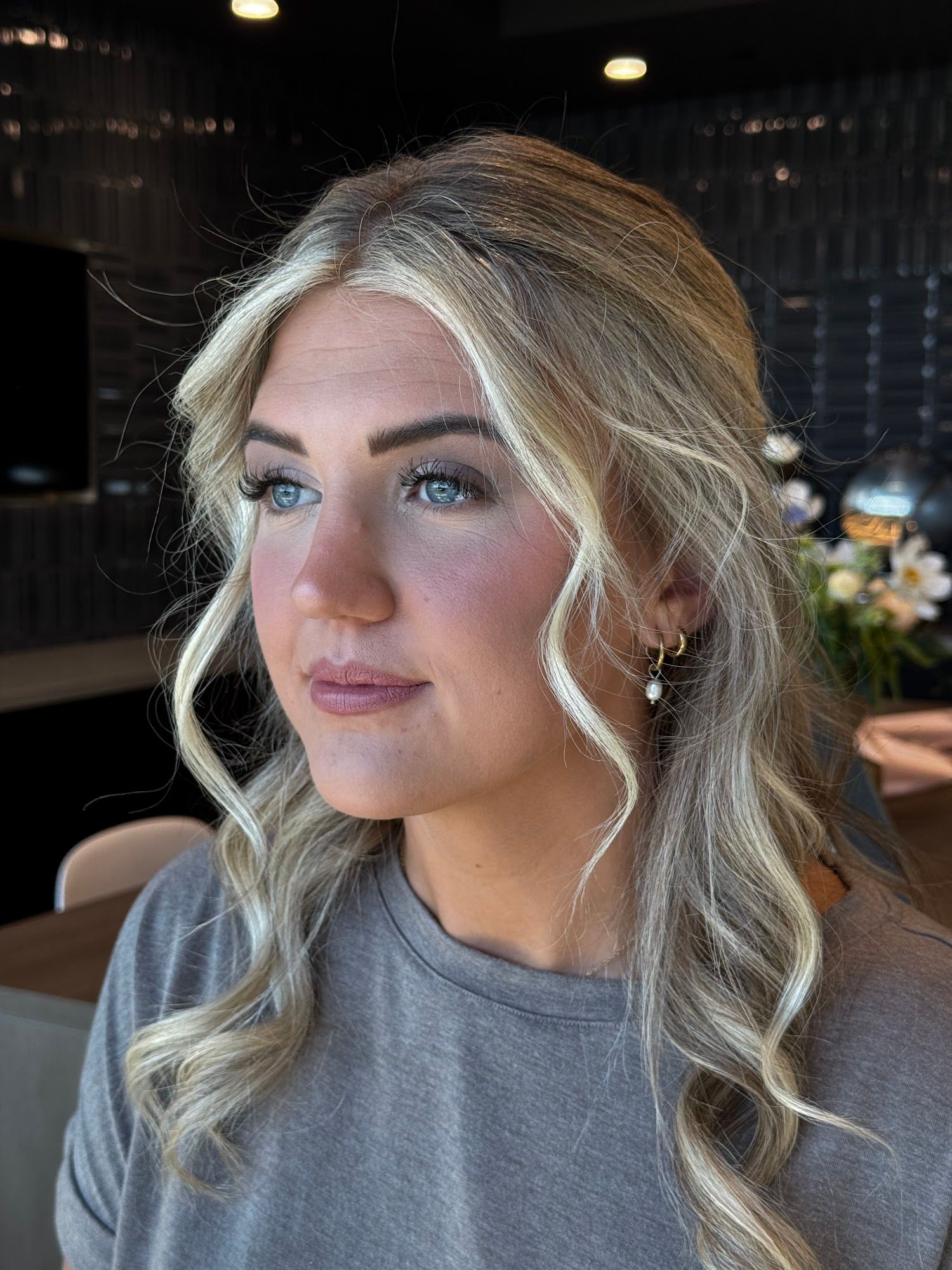 A blonde woman with loose waves and finished soft glam makeup, looking to the side