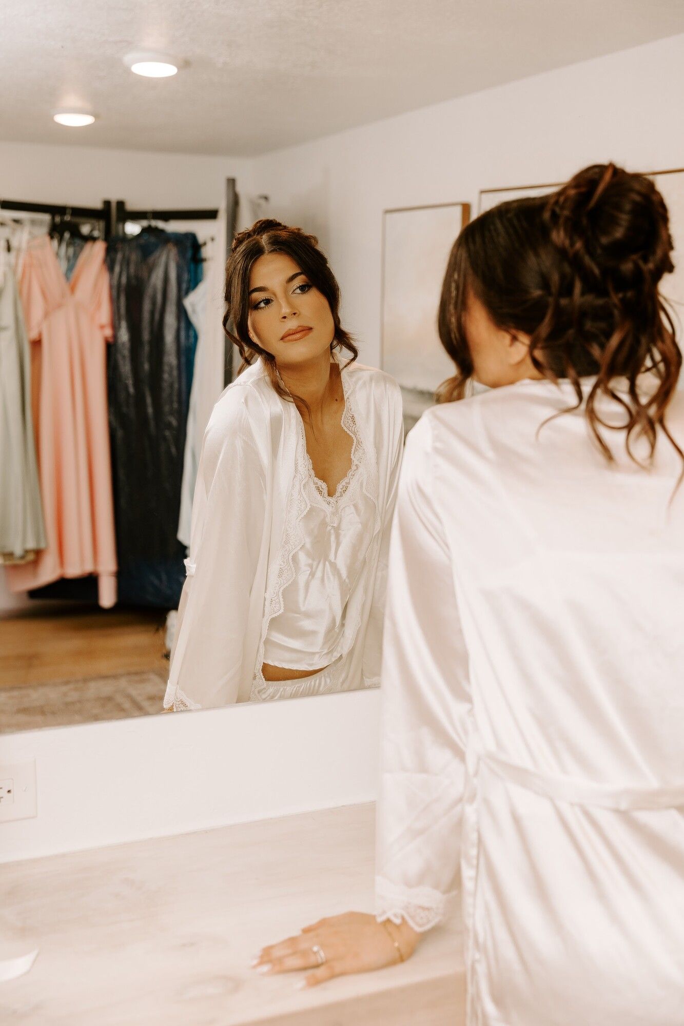 A bride in a white robe and her bridesmaid at the mirror while getting ready