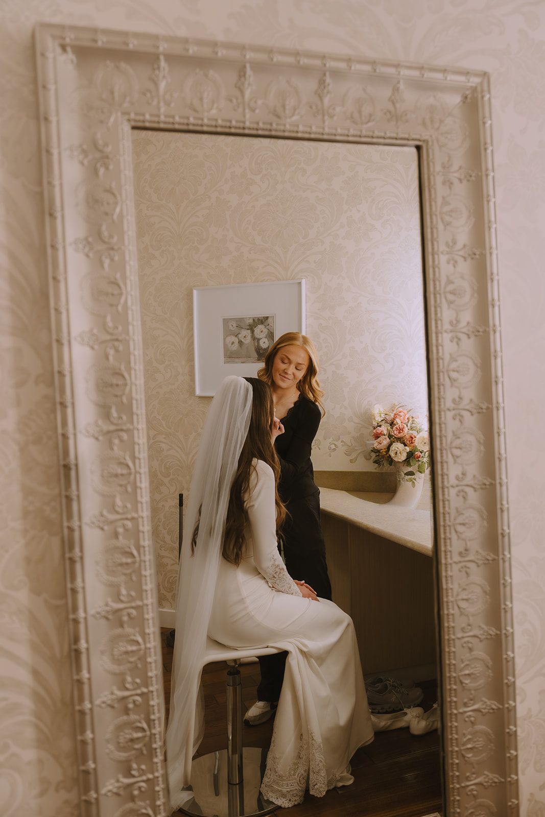 A bride in her veil reflected in an ornate mirror while getting ready, warm light