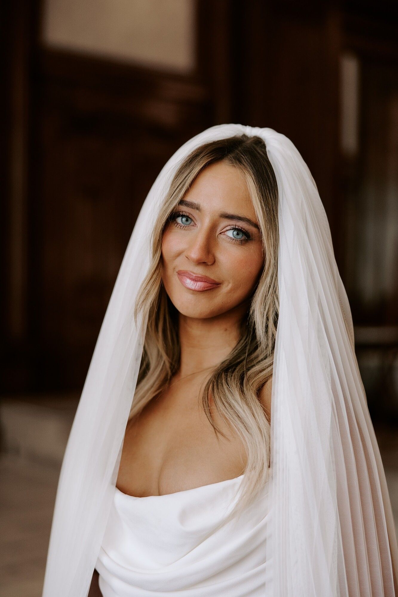 A bride in a long veil with loose blonde waves, soft glam makeup and a glowing finish