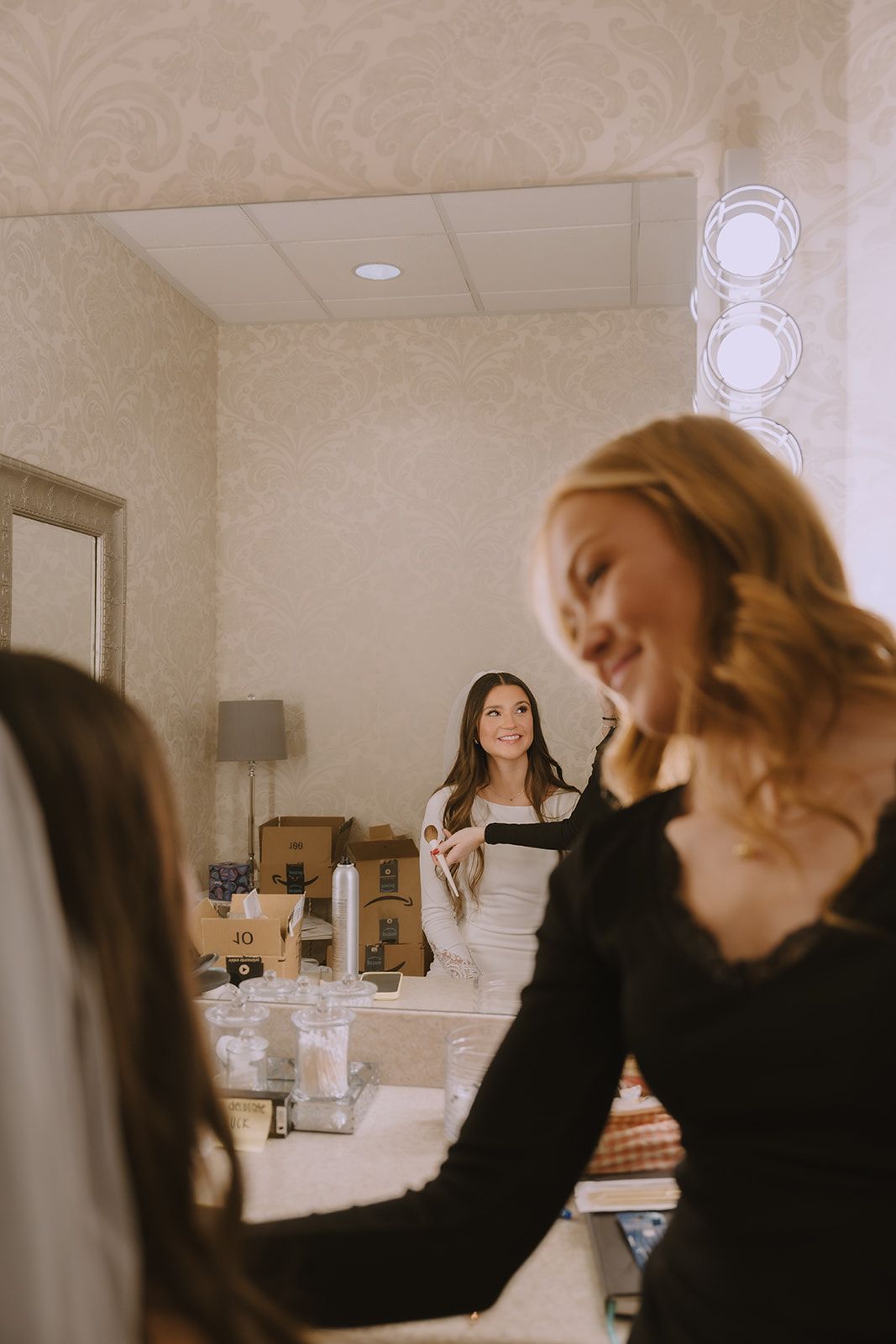 Brynlie applying makeup to a seated bride in a getting-ready room, kit open on the table