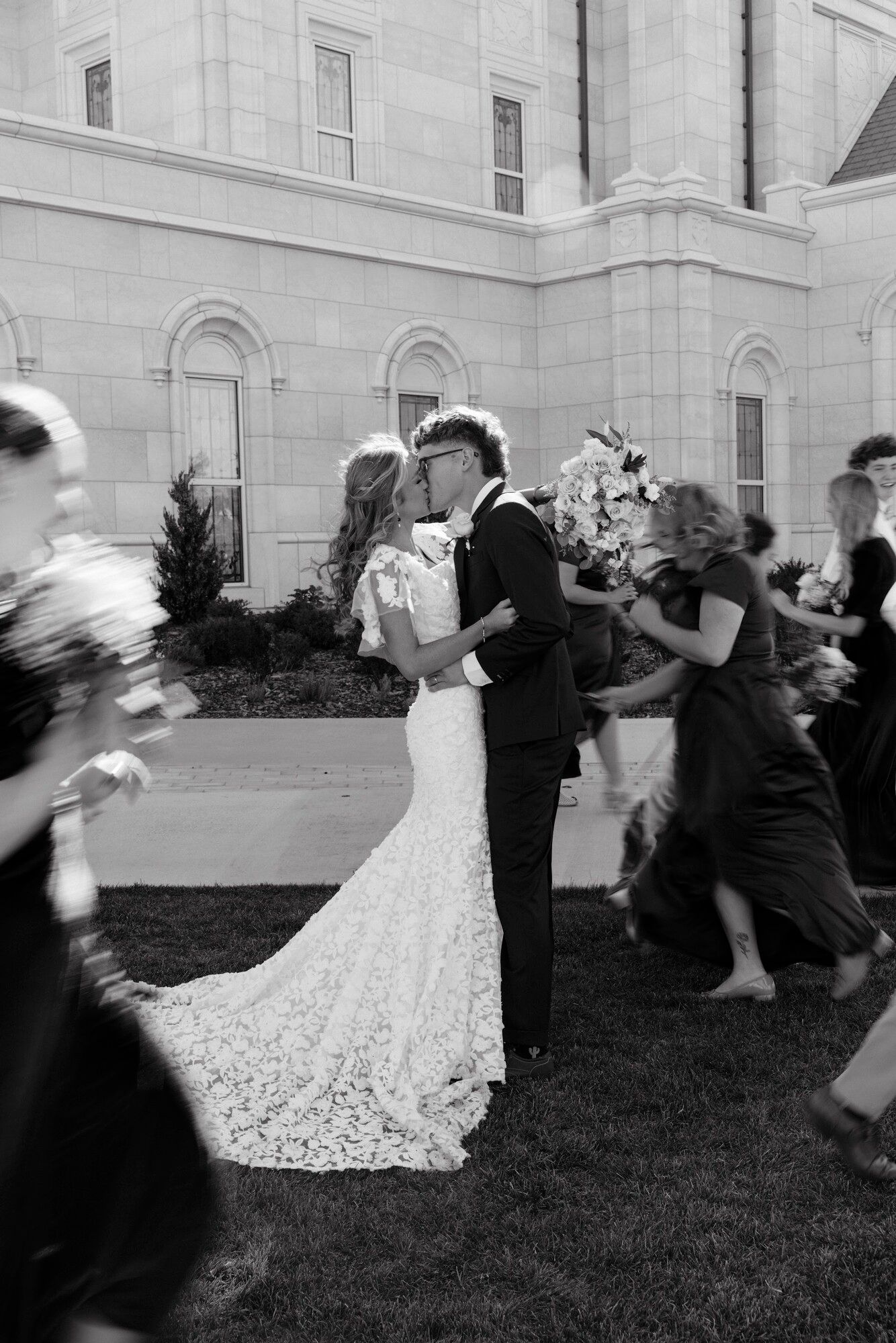 Brynlie and her husband on their wedding day in 2024, in black and white, kissing outside the temple as guests pass by