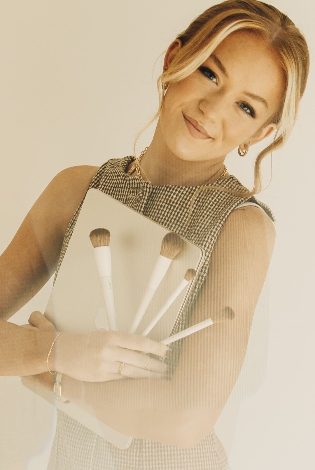 Brynlie Peay smiling at the camera, holding a handful of makeup brushes against a plain backdrop