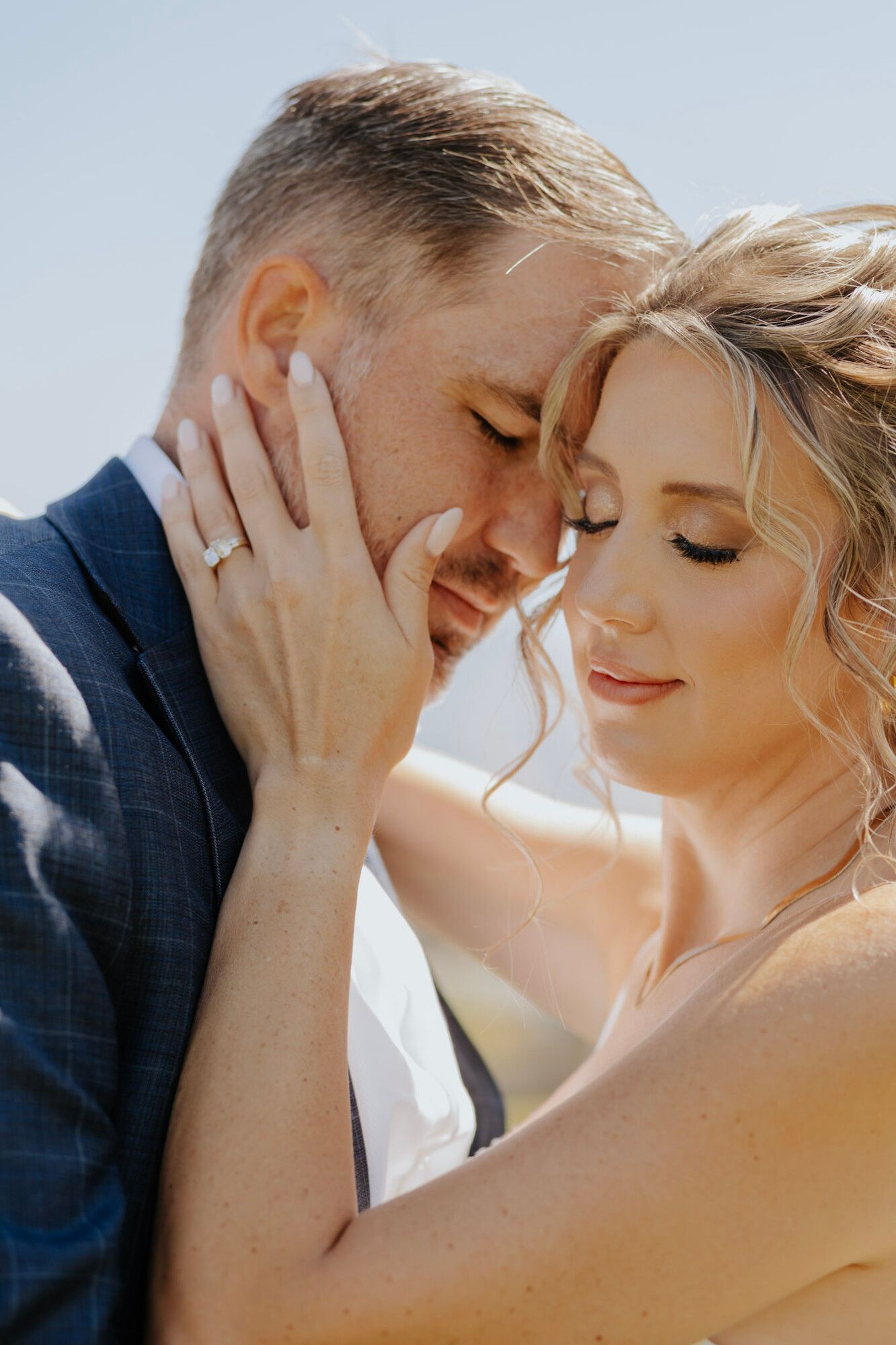 A bride with her eyes closed resting her hand on the groom's cheek, her soft glam makeup in warm light