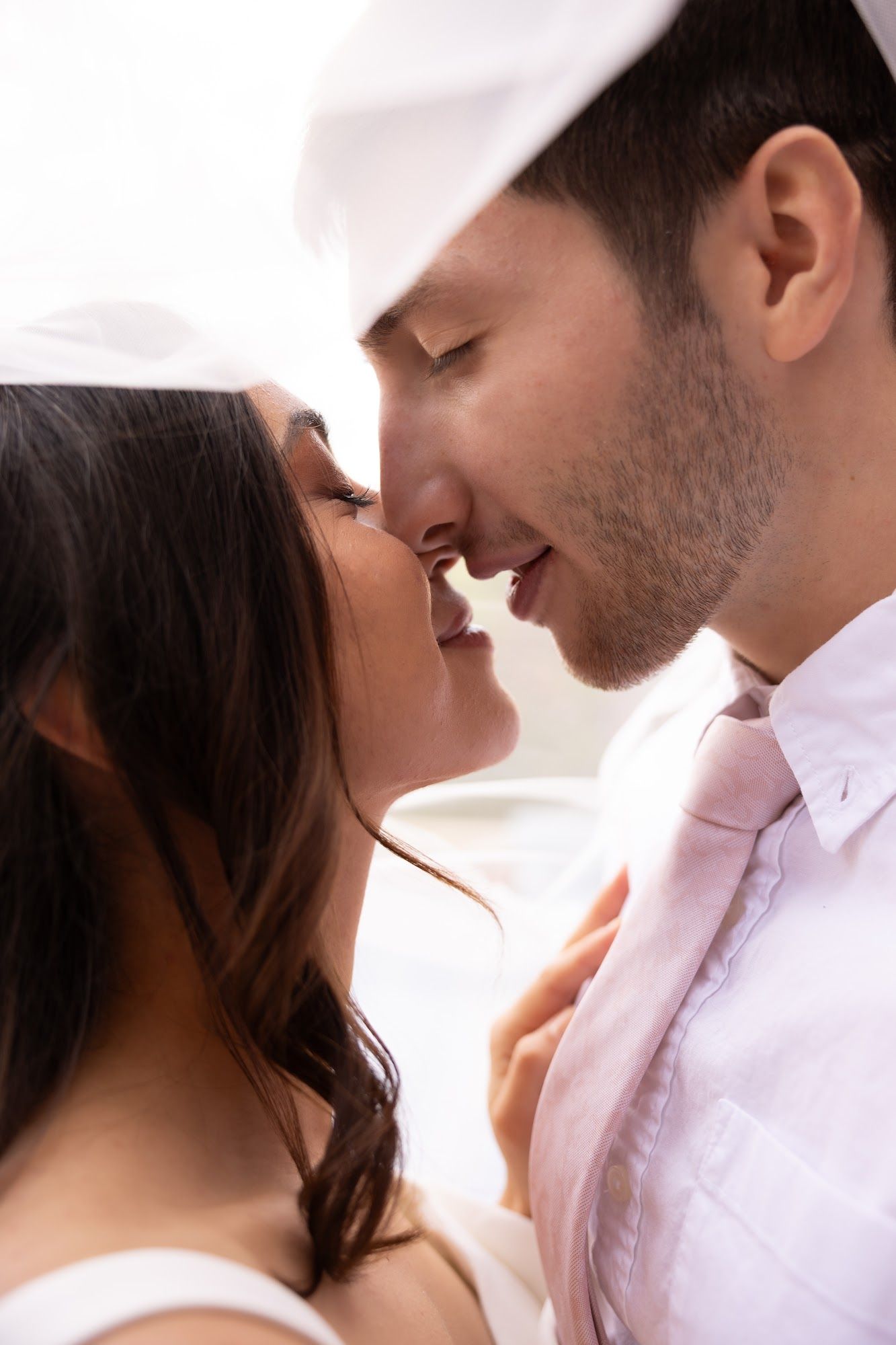 A bride under her veil, forehead to forehead with the groom, soft glam makeup in warm light