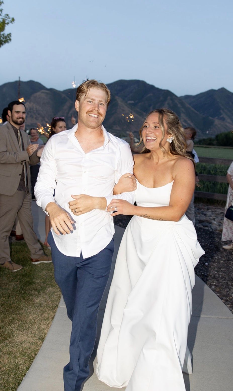A bride and groom walking out arm in arm at dusk with mountains behind them