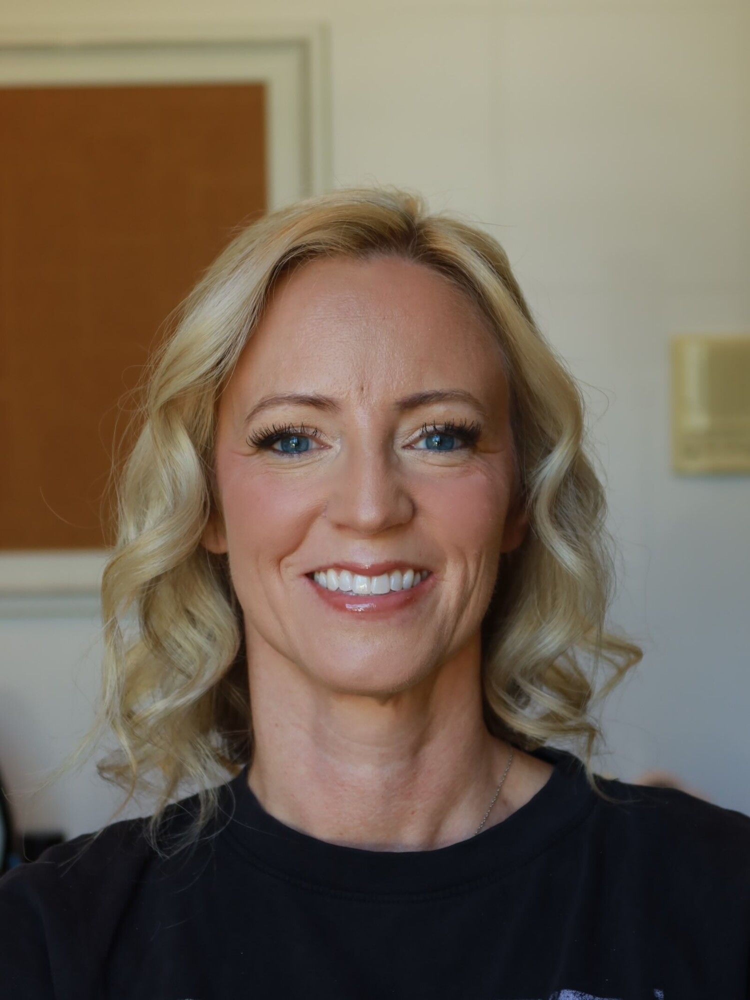 A mother of the bride smiling in soft, fresh makeup with lifted lashes and softly curled blonde hair