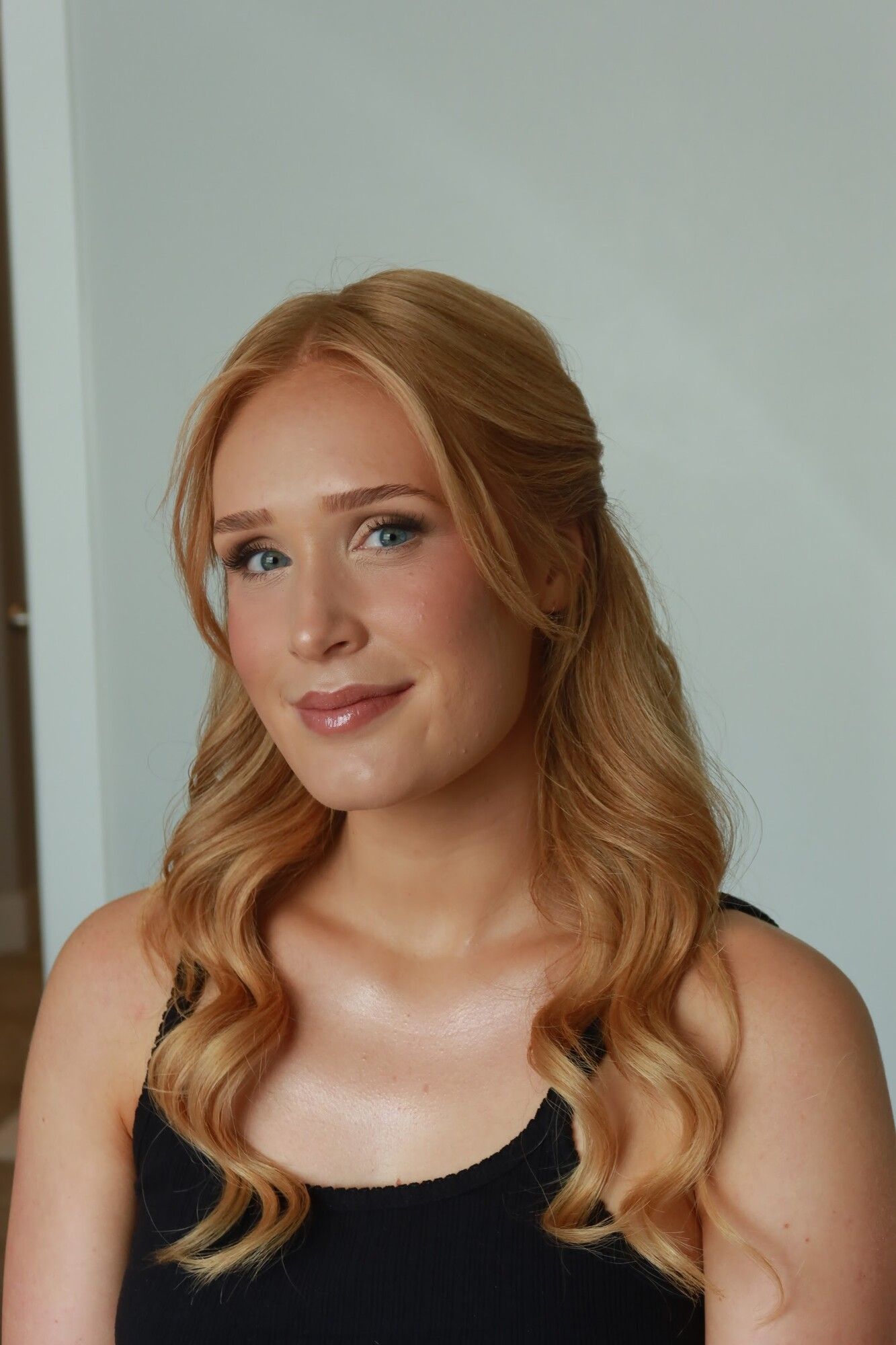 A red-haired woman with soft waves and finished soft glam makeup in a black top