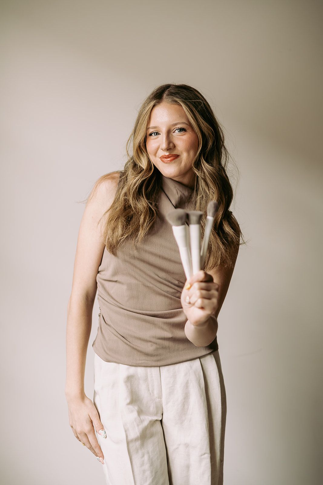 Samantha, assistant makeup artist, in a taupe top holding makeup brushes